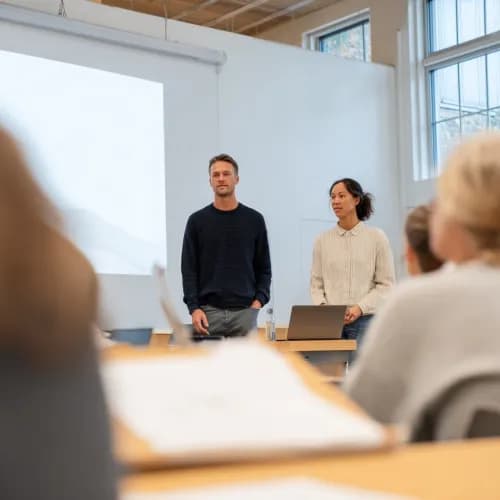 Två personer som ska hålla en kurs står längst fram i en kurslokal och håller låda. 